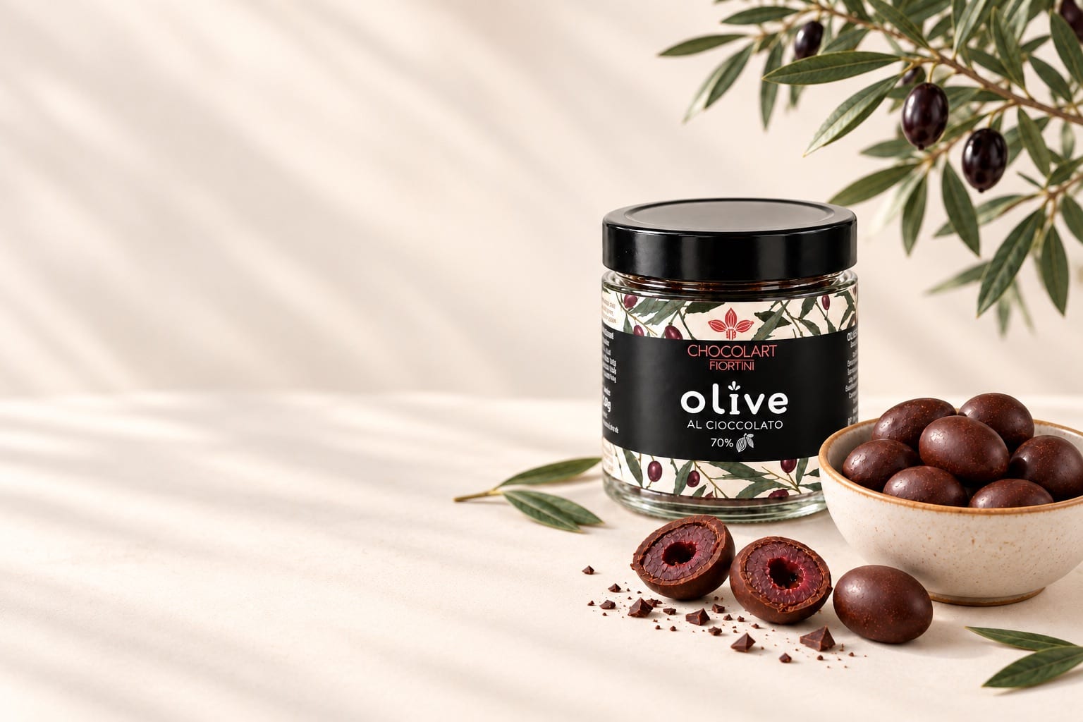 Barattolo di olive al cioccolato con una ciotola di olive ricoperte e un ramo d’ulivo