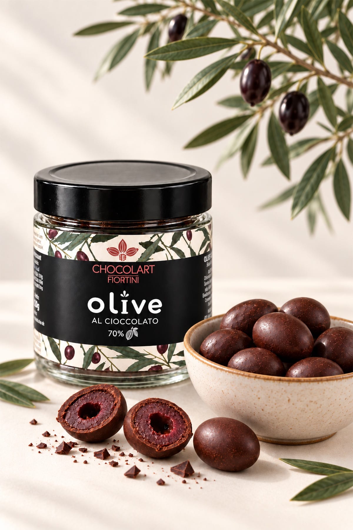 Barattolo di olive al cioccolato con una ciotola di olive ricoperte e un ramo d’ulivo